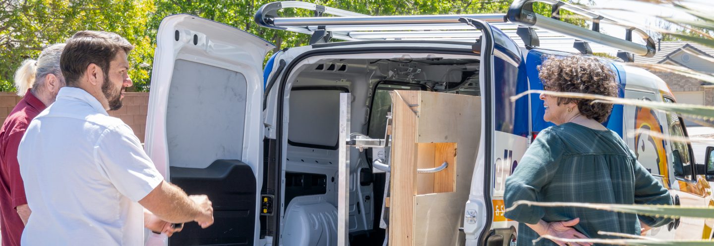 A service technician talking with a homeowner couple at the open rear doors of a work van